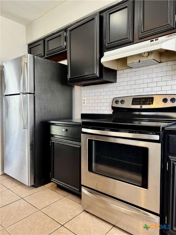 6430 Ridge Village Dr, San Antonio, TX 78233 - kitchen featuring appliances with stainless steel finishes, light tile patterned floors, dark cabinets, under cabinet range hood, and decorative backsplash