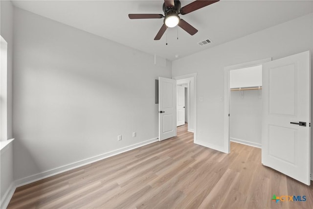 unfurnished bedroom featuring ceiling fan, a spacious closet, light hardwood / wood-style flooring, and a closet