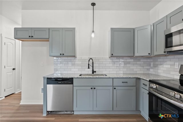 kitchen with appliances with stainless steel finishes, light stone counters, gray cabinetry, sink, and hanging light fixtures