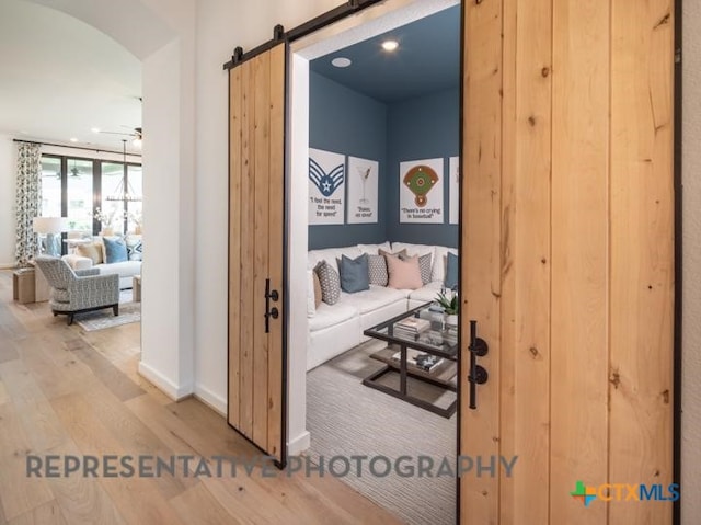 hallway with wood finished floors, a barn door, baseboards, and arched walkways