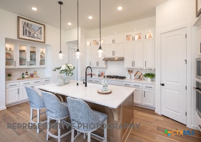 kitchen featuring a sink, stainless steel gas stovetop, under cabinet range hood, light wood-style floors, and a kitchen breakfast bar