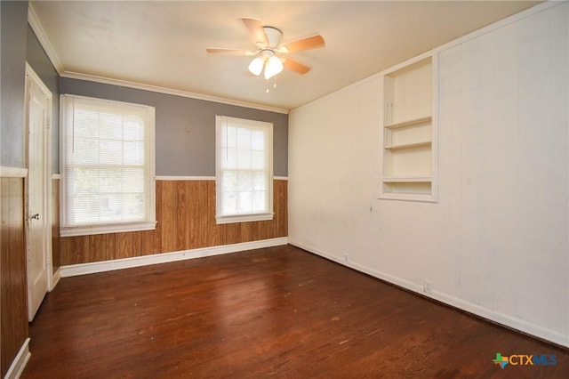 empty room with crown molding, wooden walls, dark hardwood / wood-style flooring, built in features, and ceiling fan