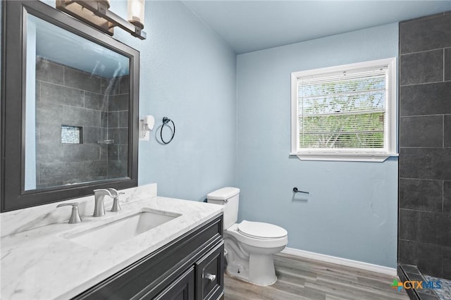 full bath with vanity, wood finished floors, toilet, baseboards, and tiled shower