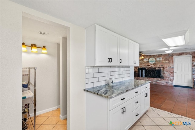 kitchen with light tile patterned floors, visible vents, white cabinets, stone counters, and a fireplace