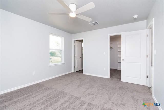 unfurnished bedroom with baseboards, visible vents, a walk in closet, and carpet flooring