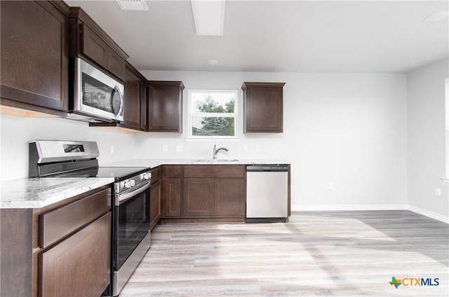 kitchen with light wood-type flooring, dark brown cabinetry, appliances with stainless steel finishes, and a sink