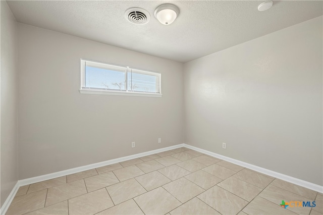 empty room with baseboards, visible vents, a textured ceiling, and light tile patterned flooring