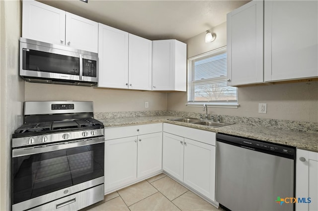 kitchen with stainless steel appliances, white cabinetry, a sink, and light stone counters