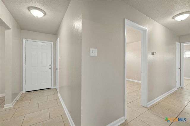 hall featuring light tile patterned flooring, a textured ceiling, and baseboards