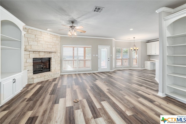 unfurnished living room featuring a stone fireplace, ceiling fan with notable chandelier, dark hardwood / wood-style floors, and crown molding