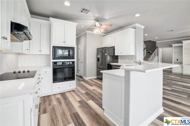 kitchen with white cabinets, kitchen peninsula, decorative backsplash, black appliances, and hardwood / wood-style flooring