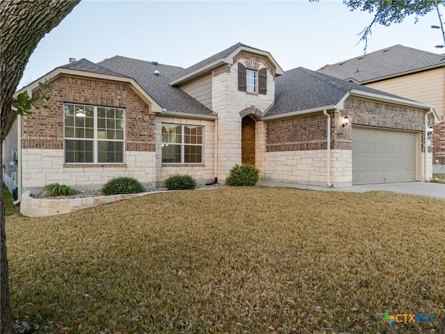 view of front of property featuring an attached garage, stone siding, a shingled roof, and a front yard