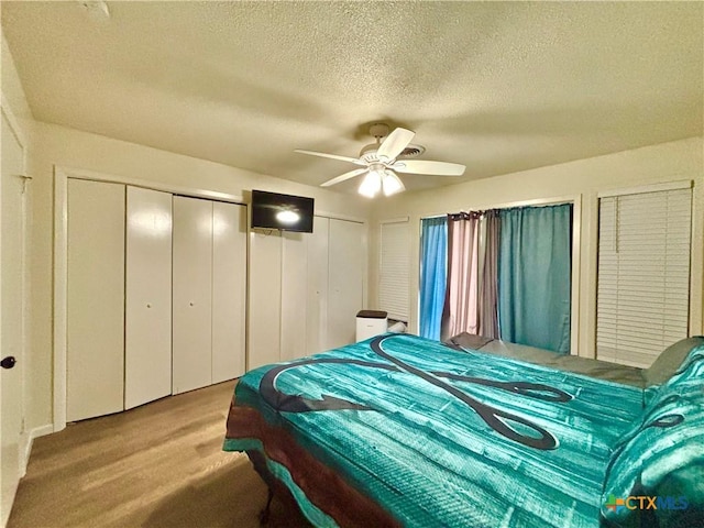 bedroom with multiple closets, ceiling fan, a textured ceiling, and light wood-type flooring