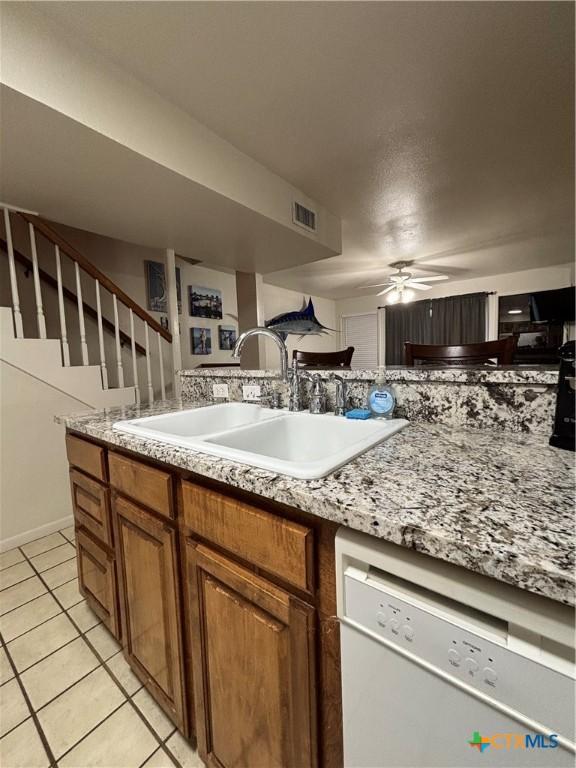 kitchen featuring light tile patterned flooring, sink, light stone counters, dishwasher, and ceiling fan