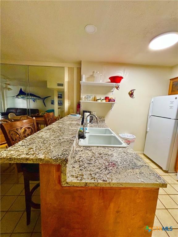 kitchen featuring white refrigerator, light tile patterned flooring, and sink