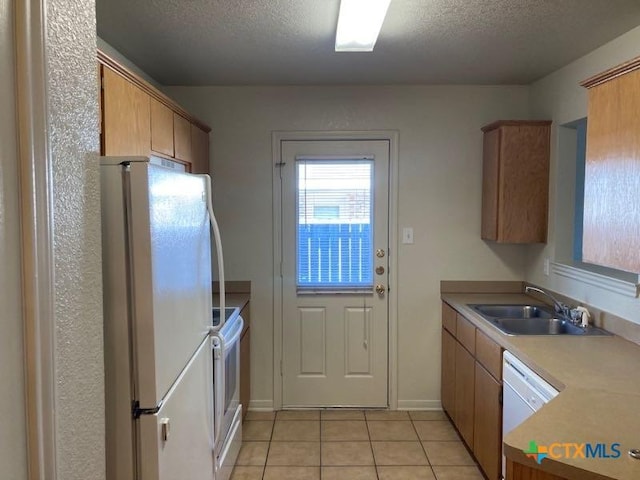 kitchen featuring a textured ceiling, white appliances, sink, and light tile patterned floors