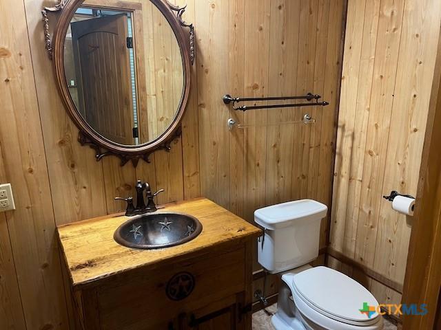 bathroom with vanity, wooden walls, and toilet