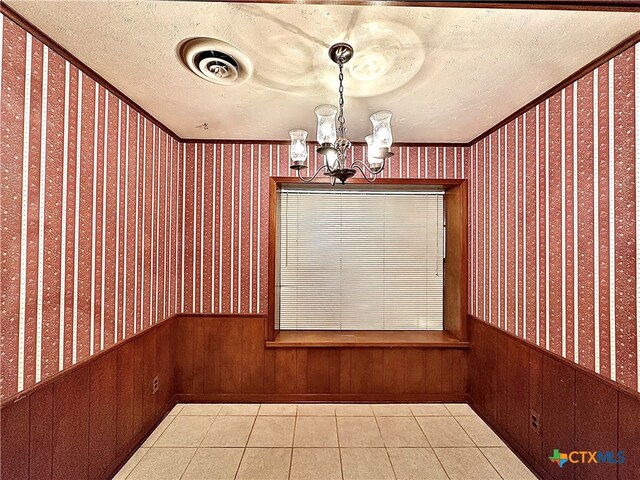 unfurnished dining area with wood walls, an inviting chandelier, light tile patterned floors, and a textured ceiling