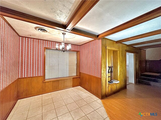 unfurnished dining area with wood walls, hardwood / wood-style flooring, beam ceiling, a textured ceiling, and a notable chandelier