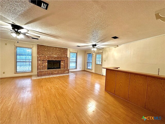 unfurnished living room with a textured ceiling, a brick fireplace, light hardwood / wood-style flooring, and a healthy amount of sunlight