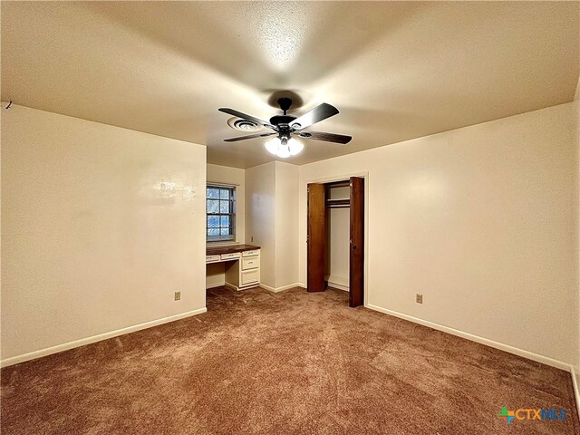 unfurnished bedroom featuring built in desk, ceiling fan, a textured ceiling, light colored carpet, and a closet