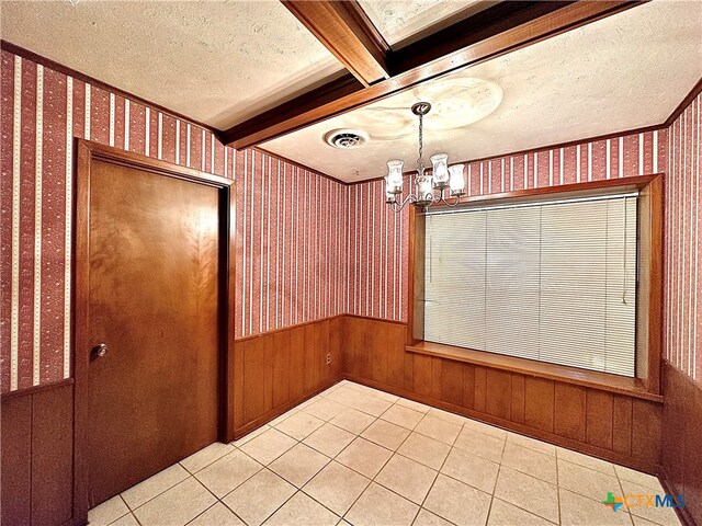 empty room featuring beamed ceiling, a textured ceiling, light tile patterned floors, an inviting chandelier, and wooden walls