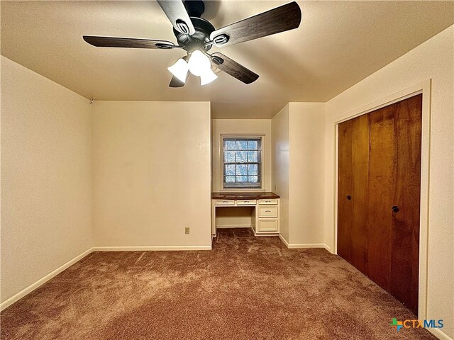 unfurnished bedroom featuring dark carpet, built in desk, and ceiling fan