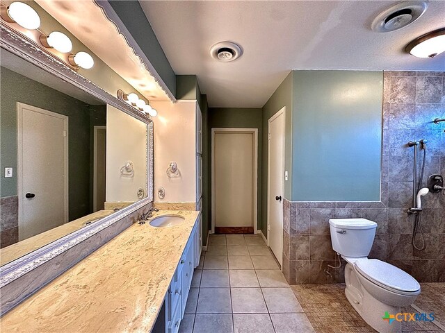 bathroom featuring tile walls, a tile shower, vanity, tile patterned flooring, and toilet