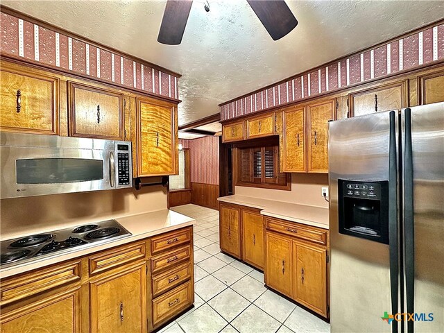 kitchen with a textured ceiling, wooden walls, ceiling fan, light tile patterned flooring, and appliances with stainless steel finishes