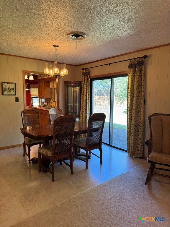 dining area featuring wooden walls, a chandelier, and a textured ceiling