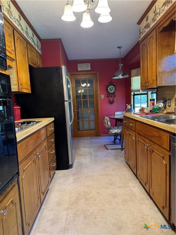 kitchen featuring a textured ceiling, stainless steel appliances, sink, a chandelier, and hanging light fixtures