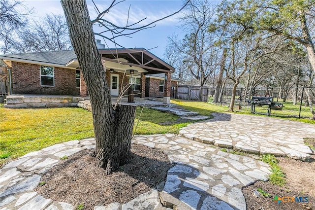 exterior space with brick siding, a ceiling fan, a patio area, fence, and a front lawn