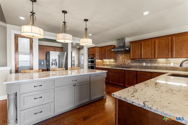 kitchen with appliances with stainless steel finishes, sink, a center island, light stone countertops, and wall chimney exhaust hood