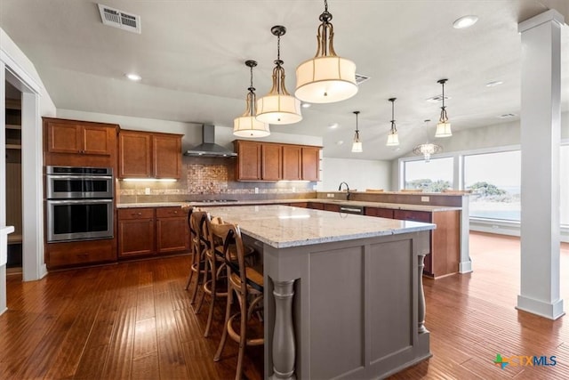 kitchen featuring pendant lighting, a breakfast bar area, double oven, a spacious island, and wall chimney exhaust hood