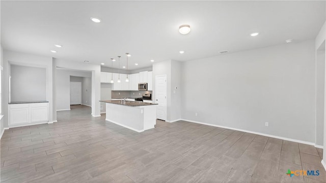 kitchen featuring stainless steel appliances, dark countertops, open floor plan, and light wood finished floors