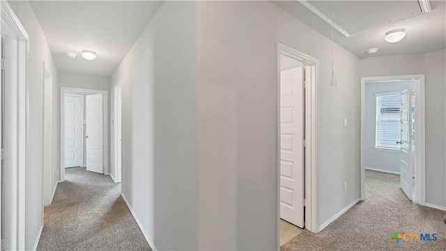 hallway with light carpet, attic access, and baseboards