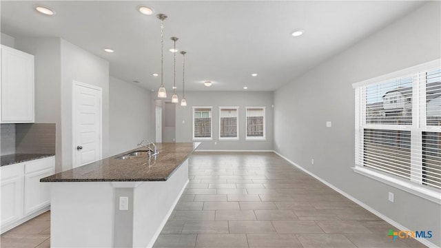 kitchen featuring dark stone countertops, a sink, a kitchen island with sink, and white cabinets