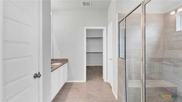 bathroom featuring a stall shower, baseboards, visible vents, a walk in closet, and vanity