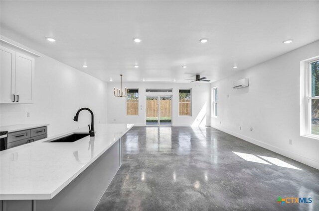 kitchen featuring ceiling fan with notable chandelier, sink, hanging light fixtures, an island with sink, and concrete flooring