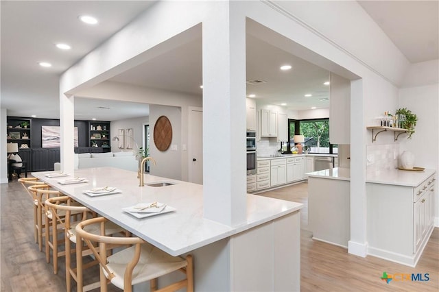 9 Mission Trce, New Braunfels, TX 78130 - kitchen featuring white cabinetry, decorative backsplash, light wood-style flooring, recessed lighting, and a breakfast bar area