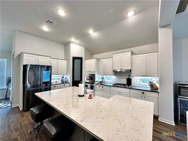 kitchen featuring sink, appliances with stainless steel finishes, a spacious island, dark hardwood / wood-style flooring, and vaulted ceiling