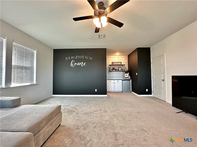 living area with a textured ceiling, light carpet, and ceiling fan