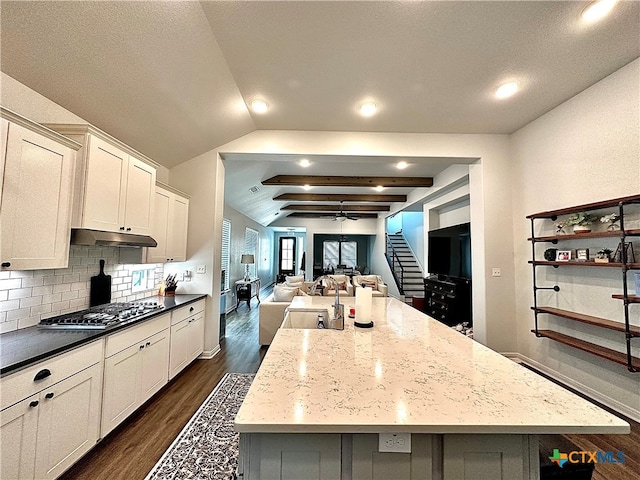 kitchen with dark stone countertops, stainless steel gas stovetop, a large island with sink, and dark hardwood / wood-style flooring