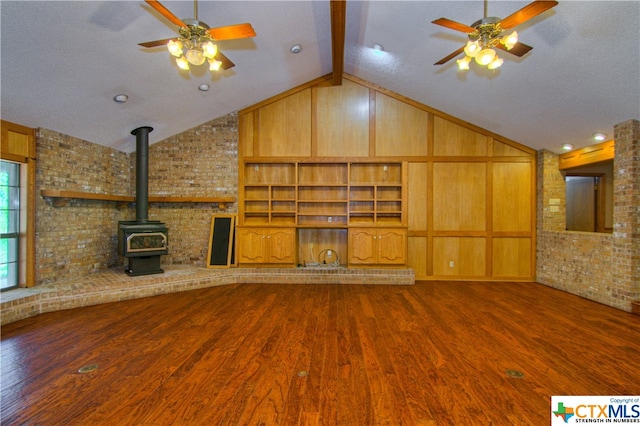 unfurnished living room with hardwood / wood-style flooring, wood walls, vaulted ceiling with beams, and ceiling fan