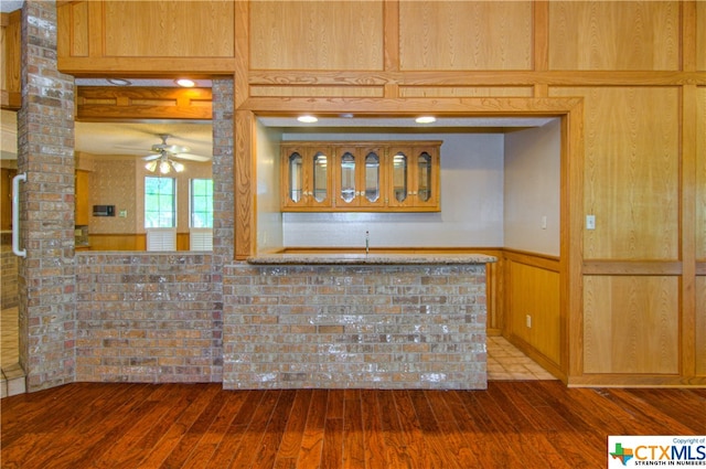 kitchen with wood walls, kitchen peninsula, hardwood / wood-style floors, and ceiling fan