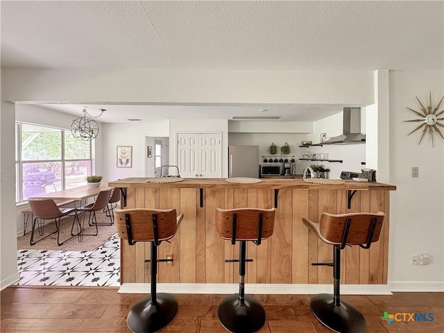149 Gallagher Dr, Canyon Lake, TX 78133 - kitchen with wall chimney exhaust hood, appliances with stainless steel finishes, a breakfast bar area, a textured ceiling, and a peninsula