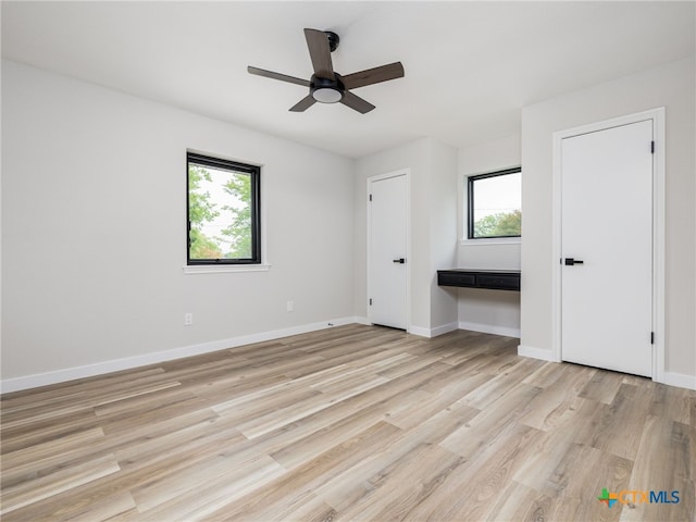 unfurnished bedroom featuring multiple windows, light wood-style floors, and baseboards