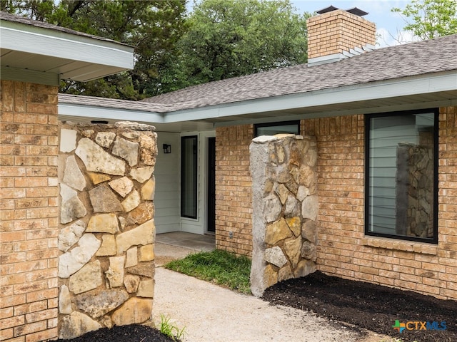 view of side of property with a shingled roof, a chimney, and brick siding