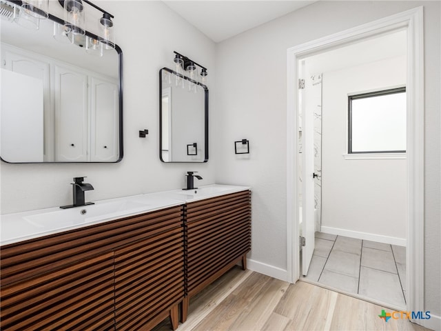 bathroom featuring baseboards, double vanity, and wood finished floors