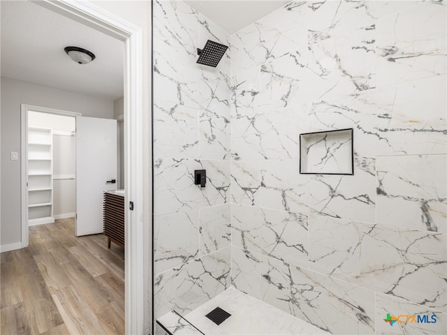 bathroom with a stall shower, wood finished floors, a walk in closet, baseboards, and vanity